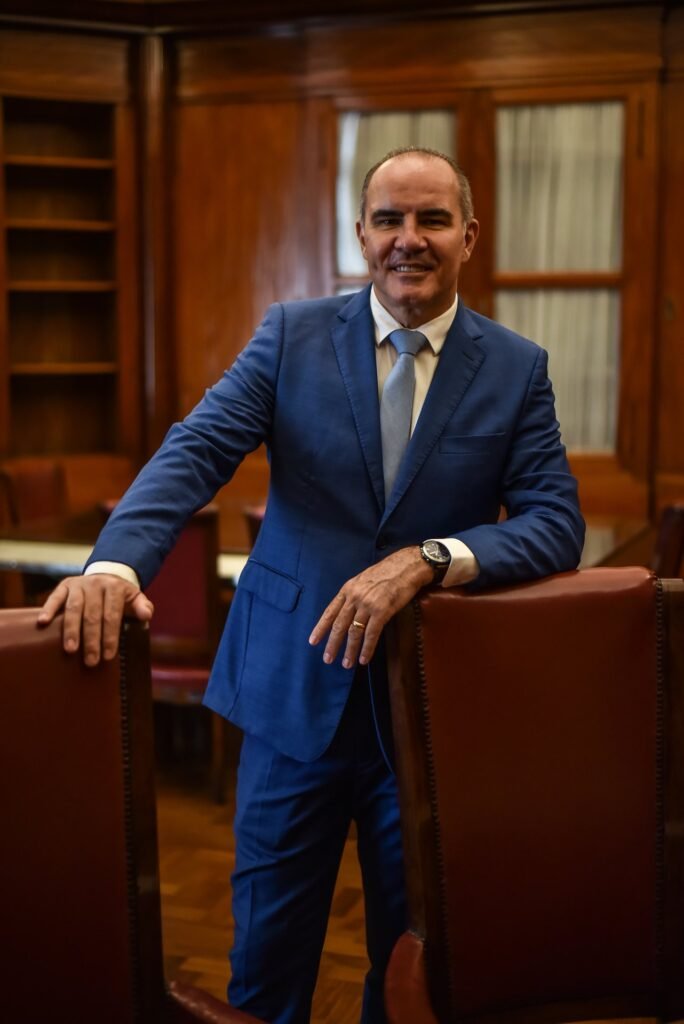 Gustavo Fernandes, advogado previdenciário, em biblioteca institucional com poltronas de couro, sorrindo com confiança