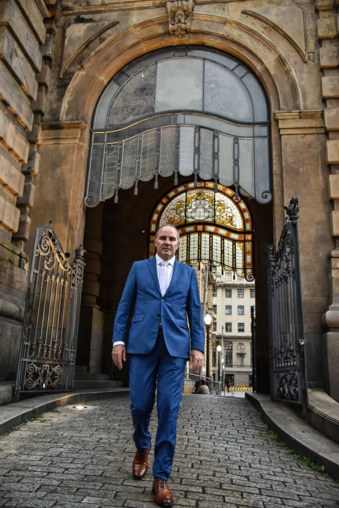 Gustavo Fernandes, advogado de direito à saúde, saindo por portal histórico com vitrais — em movimento e urgência