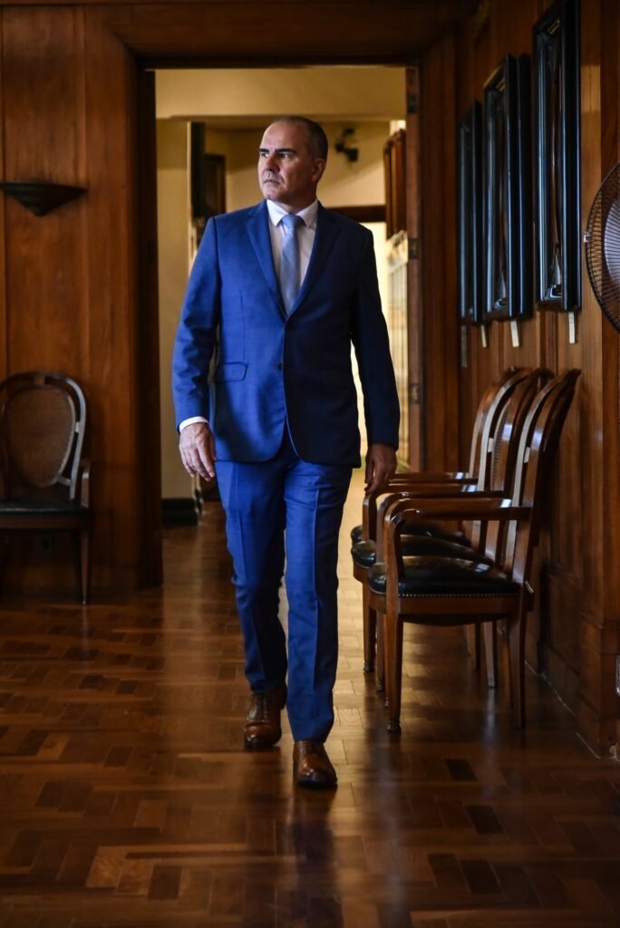 Gustavo Fernandes, advogado trabalhista, caminhando em corredor institucional clássico